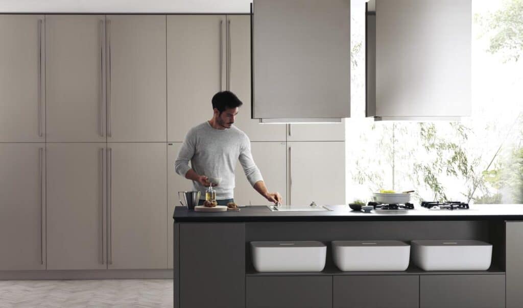 A person cooking in a modern kitchen with light gray cabinets and a large central island.