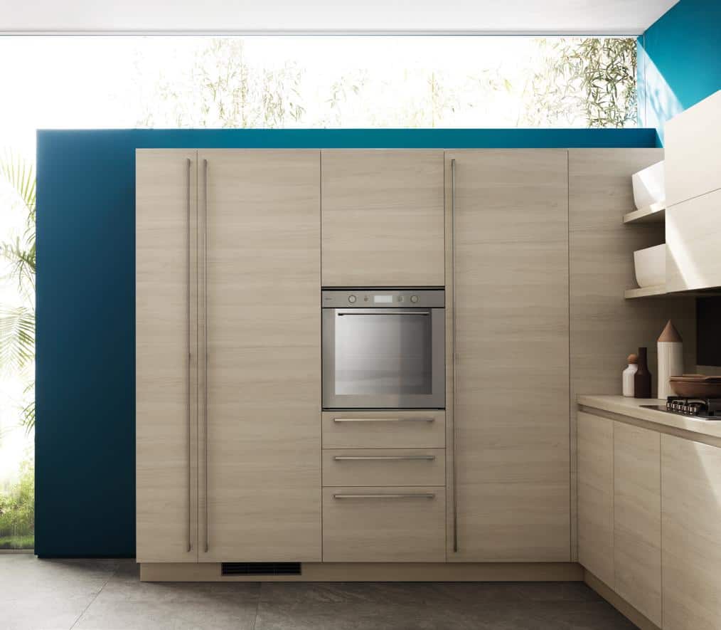 Modern kitchen with light wood cabinetry, built-in stainless steel oven, and blue accent wall.