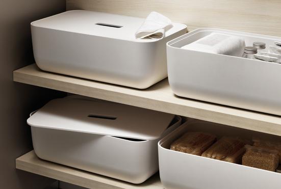 White storage boxes with lids on a wooden shelf, containing various items like bottles and sponges.