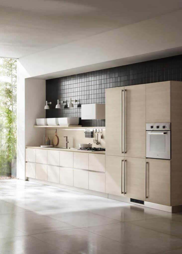 Modern kitchen with light wood cabinets, built-in appliances, and dark tiled backsplash, adjacent to a large window with outdoor view.