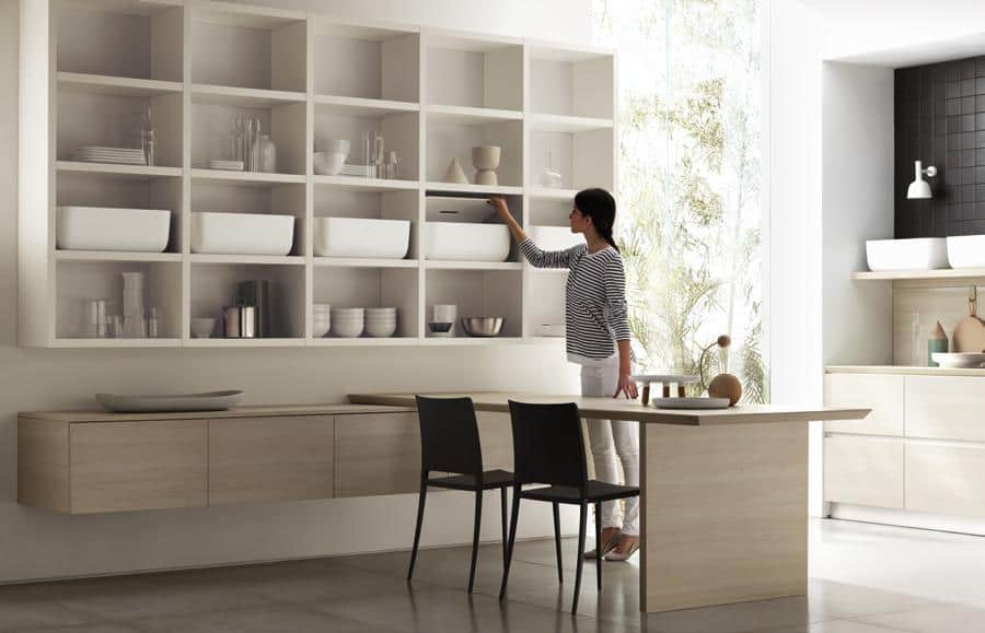 A woman reaching for a shelf in a modern kitchen with open shelving and minimalist decor.