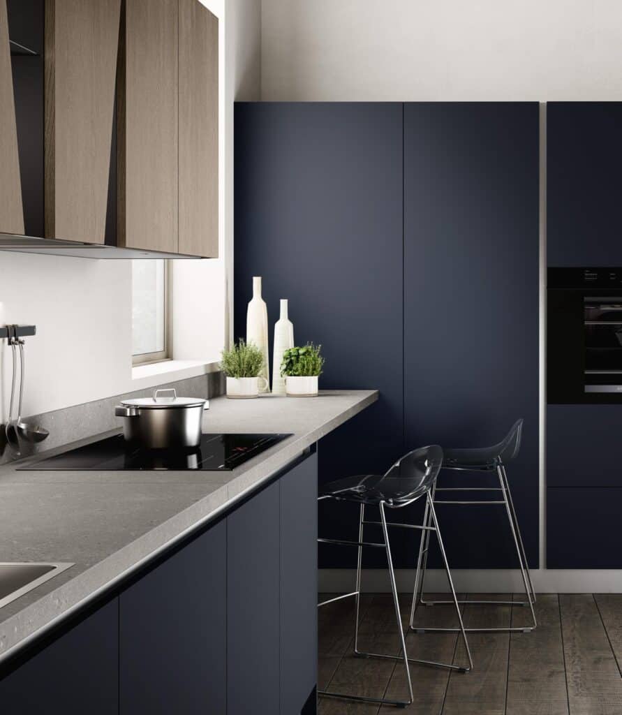 Modern kitchen with dark cabinetry, a gray countertop, an induction cooktop with a pot, two clear bar stools, and decorative plants and bottles on the counter.