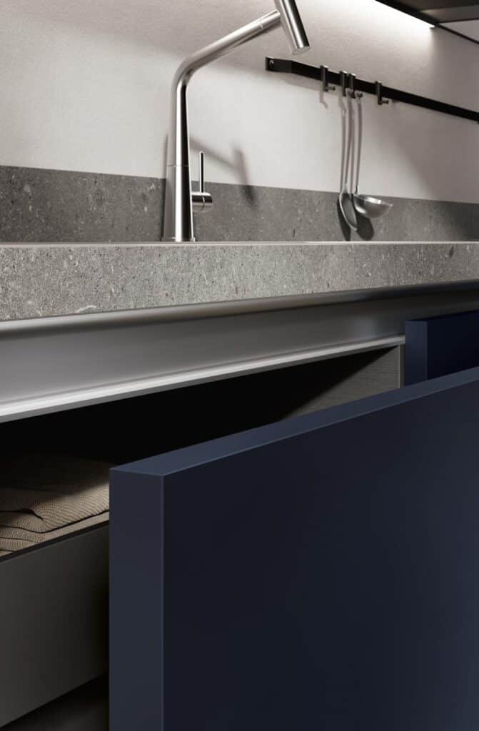 Modern kitchen with a sleek faucet, gray countertop, and open dark blue cabinet drawer.