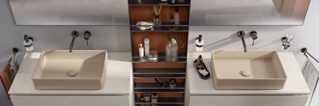 Modern bathroom with two beige rectangular sinks, wall-mounted faucets, and a central shelving unit displaying toiletries and decor.