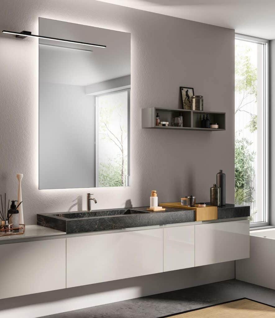 Modern bathroom with a large mirror, sleek countertop sink, and floating vanity, featuring decorative items on shelves and natural light from a large window.