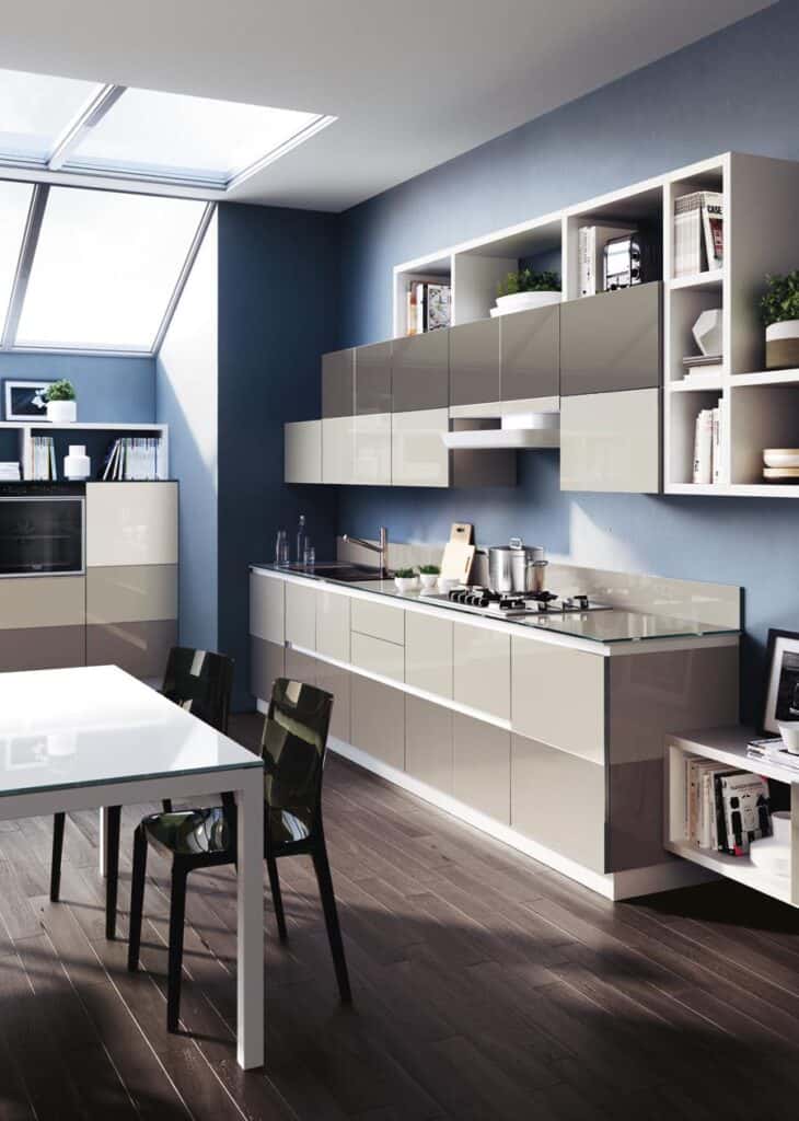 Modern kitchen with glossy cabinets, wood flooring, skylight, and a dining table with black chairs.