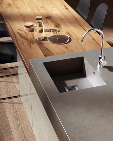 Modern kitchen interior with a stone countertop, integrated sink and faucet, and adjacent wooden table set with glass bottles and cork lids.