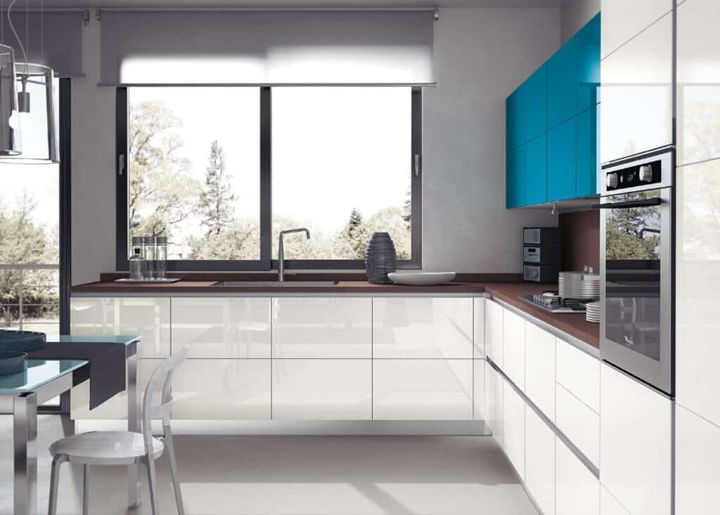 Modern kitchen with glossy white cabinets, blue upper cabinets, a built-in oven, and a large window providing natural light.