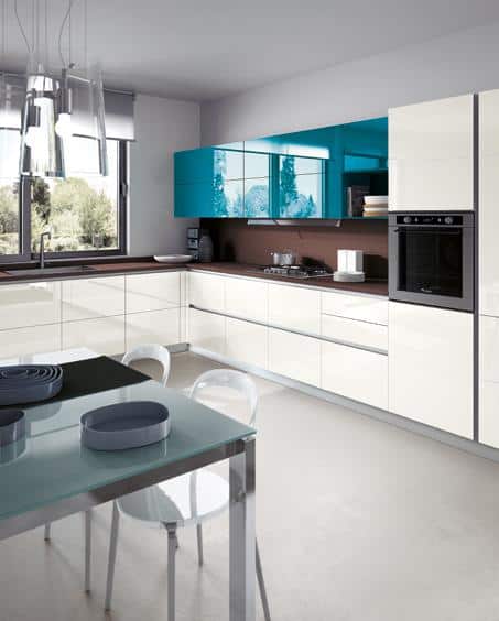 Modern kitchen interior with glossy white cabinets, turquoise upper cabinets, a glass dining table, and built-in appliances.