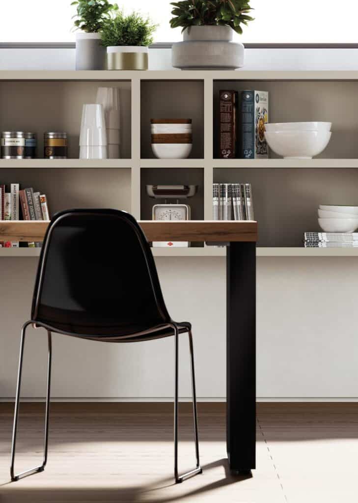 A modern kitchen interior with a black chair, a wooden table, and shelves displaying books, bowls, potted plants, and assorted kitchen items.