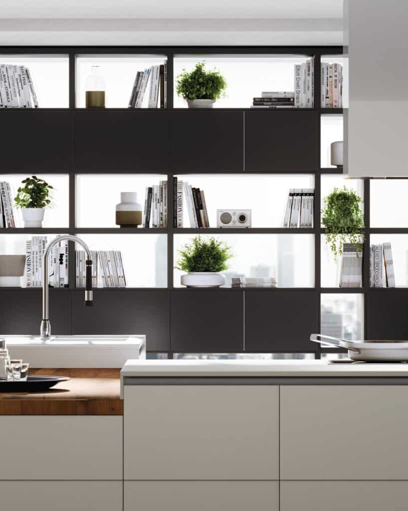 Modern kitchen interior with open shelving, books, potted plants, and a sleek faucet over a white counter.