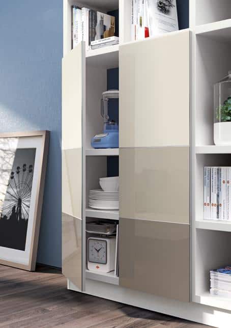Modern shelving unit with beige glossy cabinet doors, containing books, a blender, plates, and a framed picture leaning against the wall.
