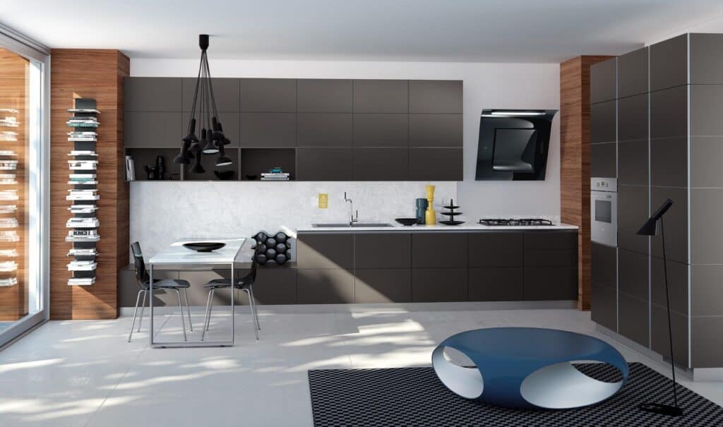 Modern kitchen with dark cabinets, a marble countertop, and a sleek black range hood. A small dining table with chairs sits in the corner, under a cluster of black pendant lights. The room features a tall bookshelf, wooden accents, and a round blue coffee table on a patterned rug.