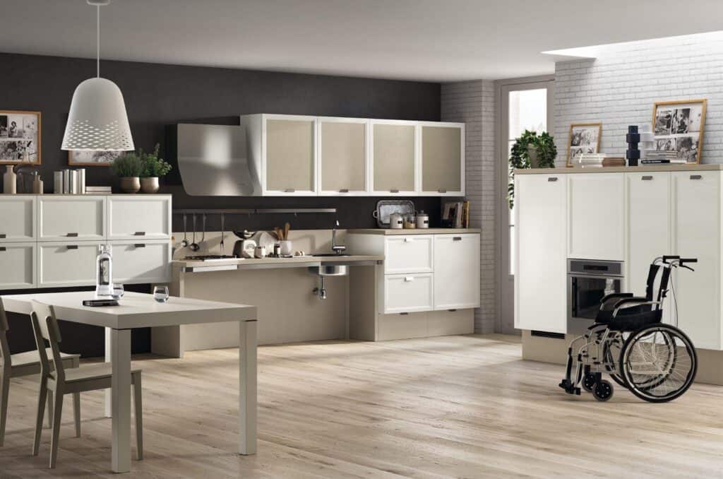 Modern kitchen with white cabinetry, accessible countertop and sink, dining table with chairs, and a wheelchair on a wooden floor.