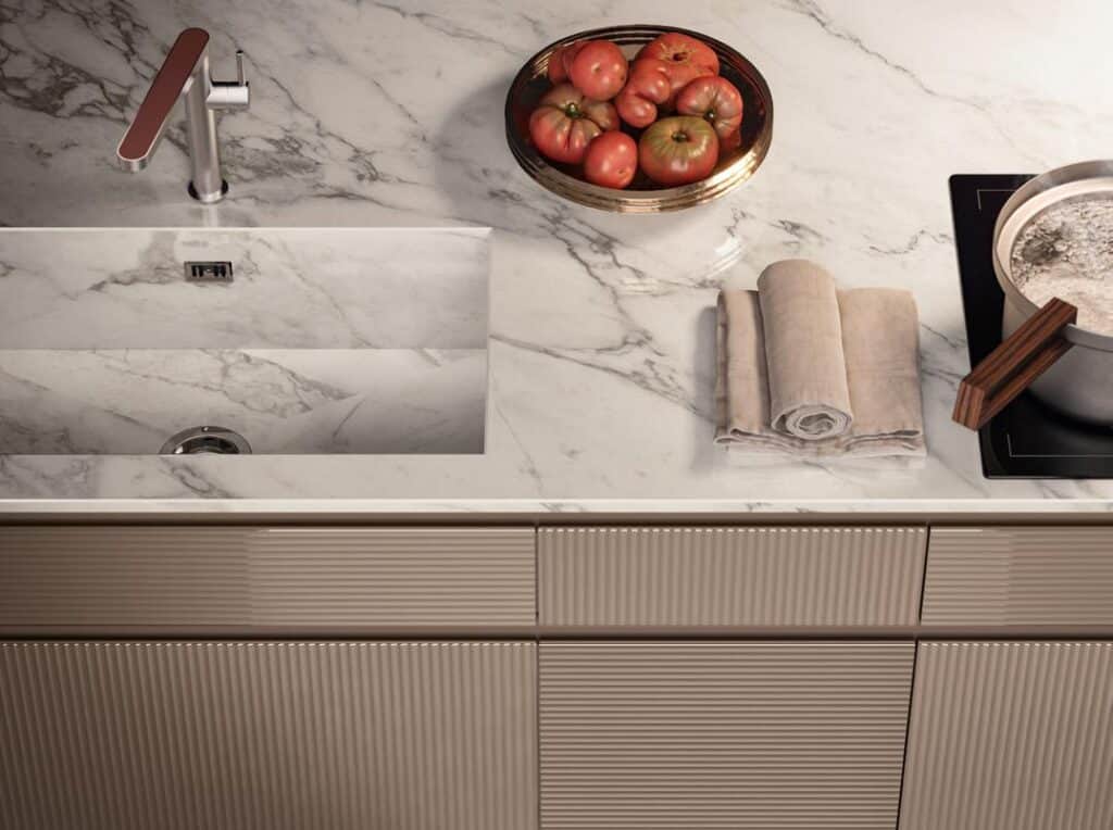 Marble kitchen countertop with built-in sink, plate of tomatoes, folded towels, and pot on an induction cooker.