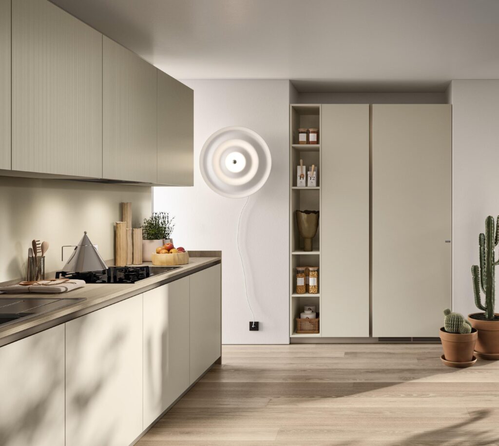 Modern kitchen with light green cabinets, wooden countertops, and a wall-mounted circular light fixture. A cactus is placed in the corner.