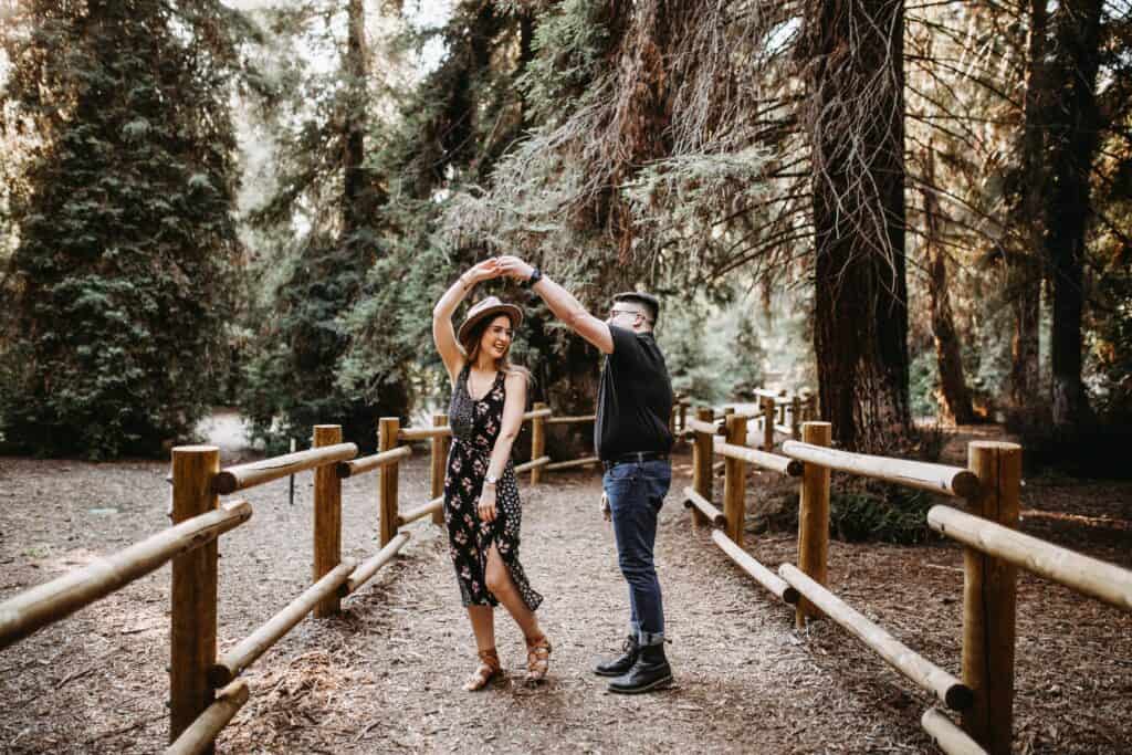 A man spinning a woman while dancing together on a wooded outdoor path