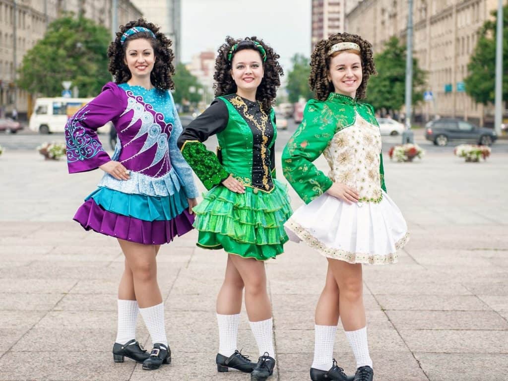 Colorful Irish dance costumes on women in cultural parade, urban background.