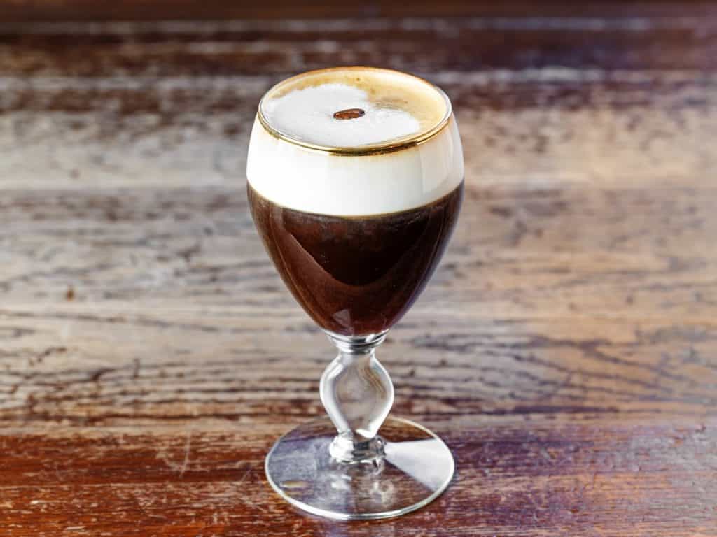 Rich Irish coffee with whipped cream and a coffee bean on top.