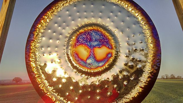 Reflective circular art with a colorful tree design at its center in an outdoor setting.
