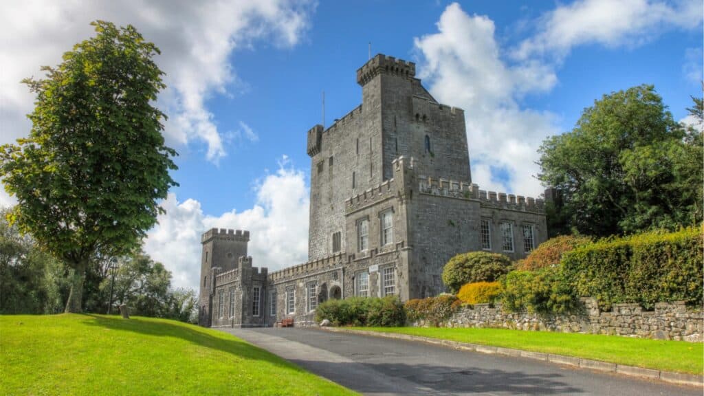Medieval castle with lush green gardens and vibrant foliage under a blue sky.