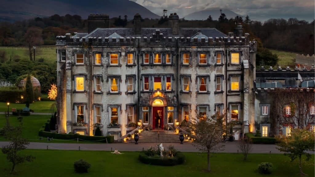 Elegant Irish castle lit at dusk, surrounded by lush gardens and scenic landscape.