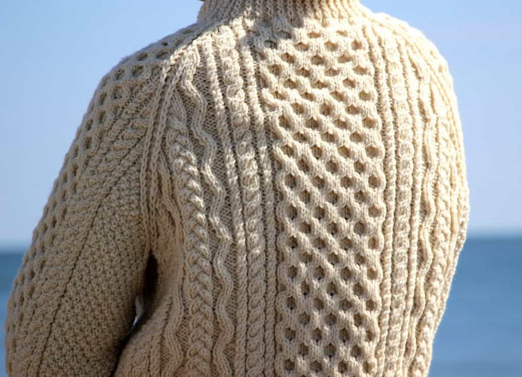 Hand-knitted cream sweater with cable patterns, outdoors against a blue sky and sea.