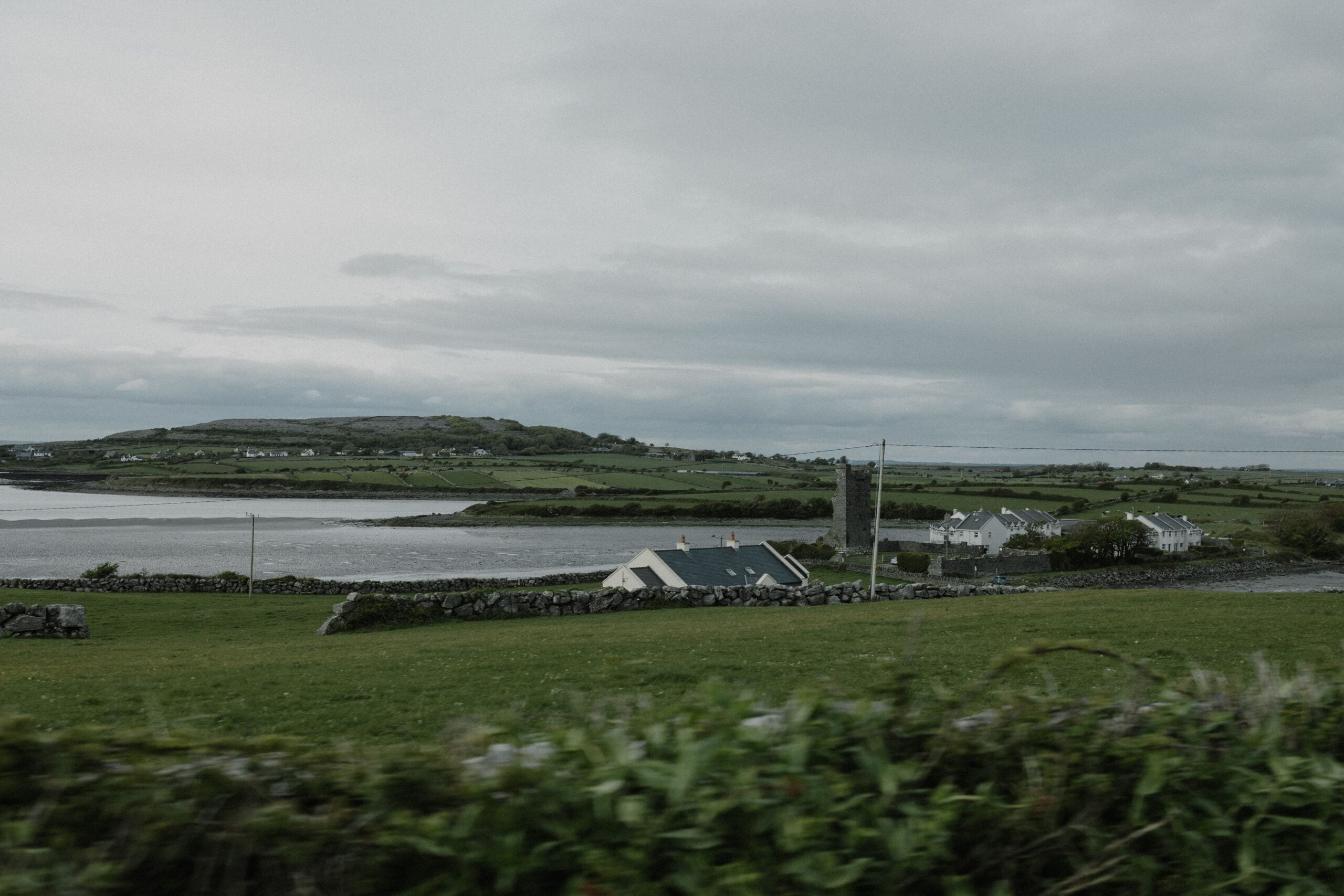 Irish countryside with lake and farm buildings under cloudy sky.