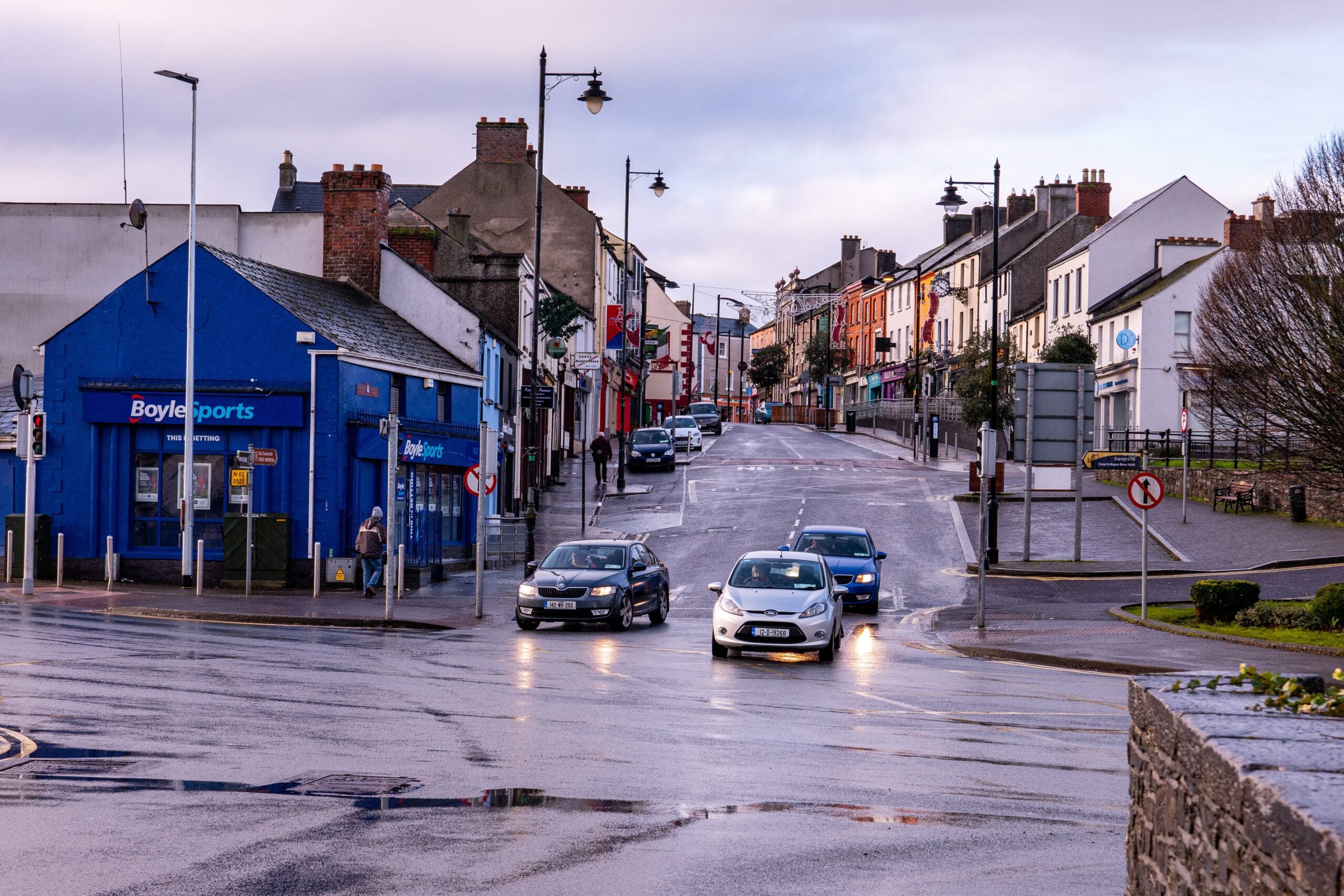 Town street in Ireland with shops and cars, rainy weather.