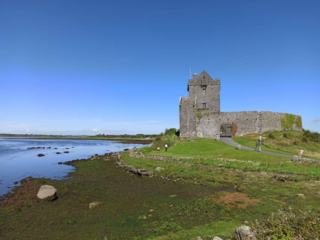 Scenic view of medieval Dunguaire Castle by Galway Bay, Ireland under a clear blue sky.