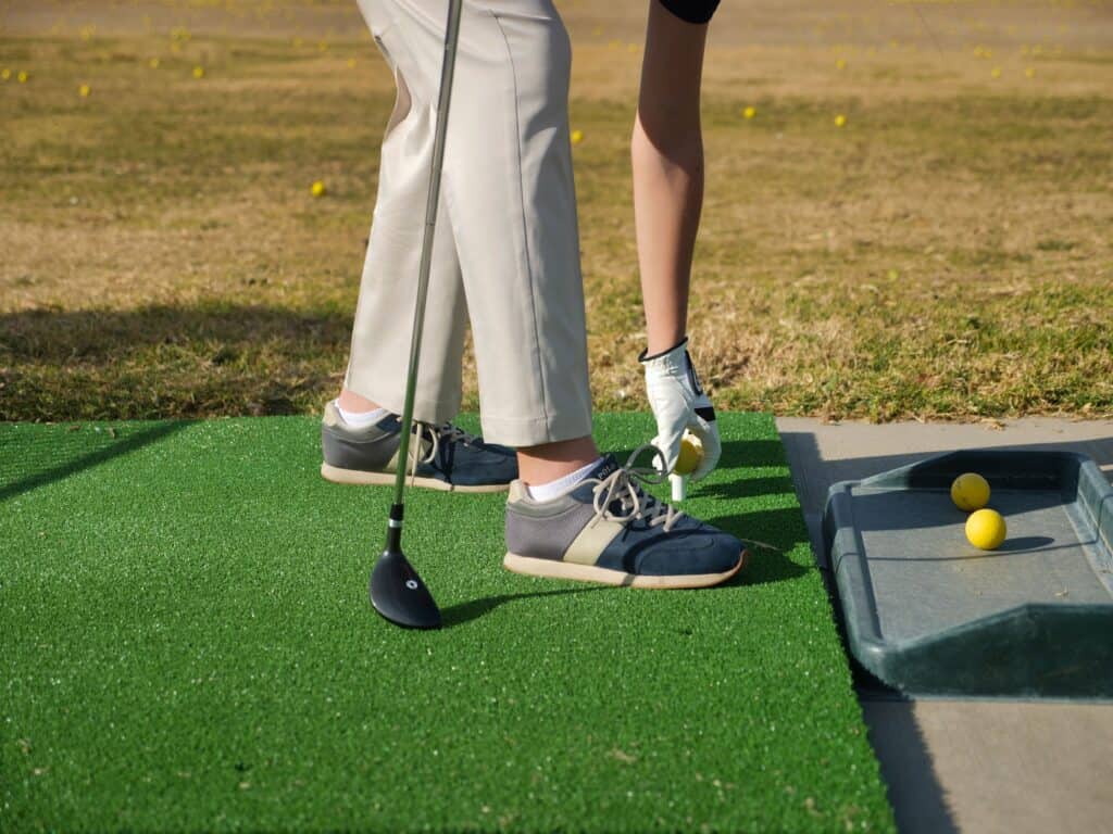 Person placing golf ball on tee at an outdoor driving range for practice.
