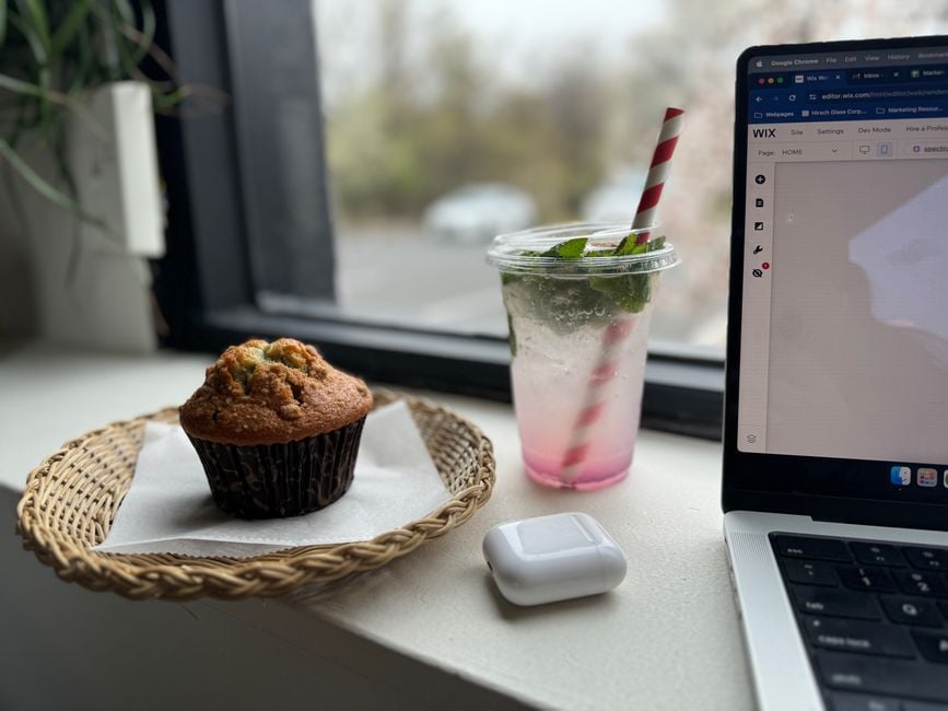 A relaxing workspace scene in a café with a muffin, drink, and laptop by the window.