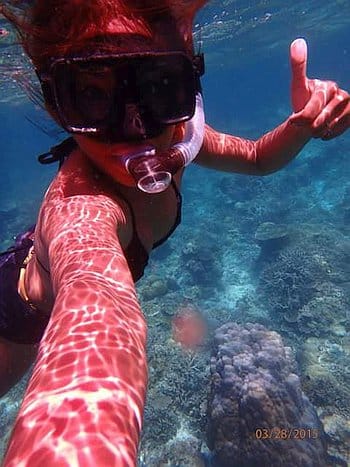 Amidst vibrant coral and crystal-clear water, a person snorkeling during a boat tour gives a cheerful thumbs-up, wearing their mask and snorkel.