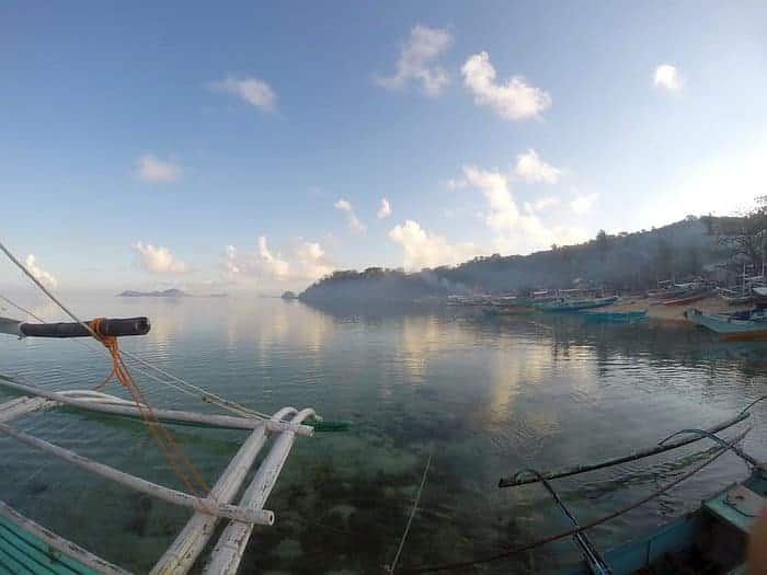 Scenic view of a calm bay with boat tours leisurely drifting by, a rocky shoreline, and a clear blue sky reflecting on the water near Barangonan.
