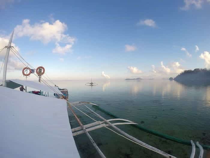 A peaceful view of calm sea water and cloudy sky, with a boat setting off for an island-hopping tour to the distant islands, perhaps even reaching Barangonan.