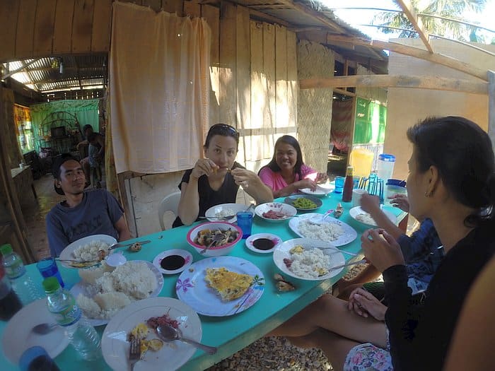 People enjoying a meal together at an outdoor table with various dishes, including rice and omelets, in a rustic setting, after an exhilarating day of island hopping.