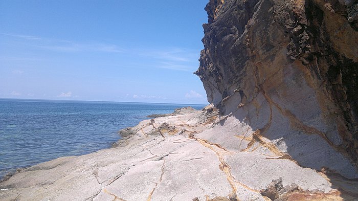 Rocky shore with a steep cliff and clear blue sea under a bright sky, perfect for an unforgettable Palawan island hopping adventure.