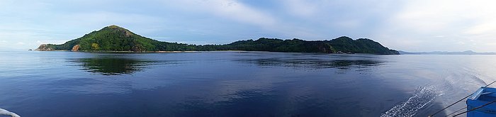 Panoramic view of a calm sea highlights a lush green island, perfect for an exhilarating boat tour, beneath a clear blue sky.