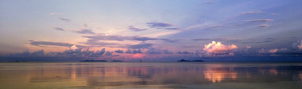 Experience a serene boat tour through the calm sea, where Palawan's islands silhouette against a vibrant sunset sky, its colors beautifully reflecting on the tranquil water.