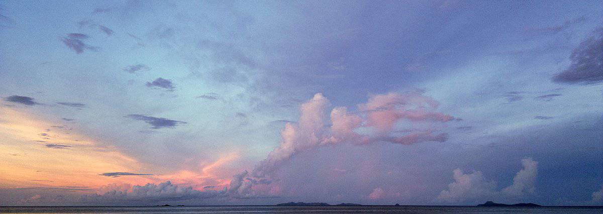 A serene sunset over the ocean with pastel pink and blue hues paints the sky, while distant clouds hover on the horizon. It's a perfect backdrop for an island hopping adventure, offering tranquil moments as you glide across the water.