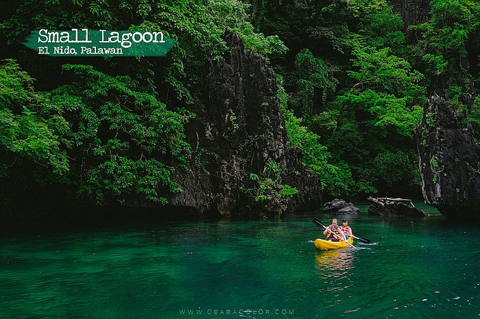 Two people paddle a kayak in the emerald waters of Small Lagoon, part of an unforgettable island hopping adventure, surrounded by lush greenery and rocky cliffs in El Nido, Palawan.