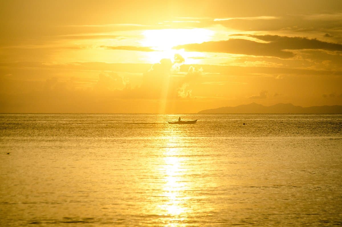 A small boat on a calm ocean at sunset, perfect for an evening boat tour, with golden sunlight reflecting on the water and silhouetted distant hills.