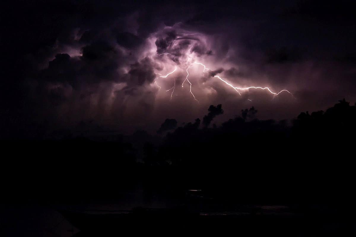 Dark sky illuminated by jagged lightning bolts through thick clouds, casting a dramatic silhouette over the landscape below, perfect for an electrifying boat tour amidst nature's fury.