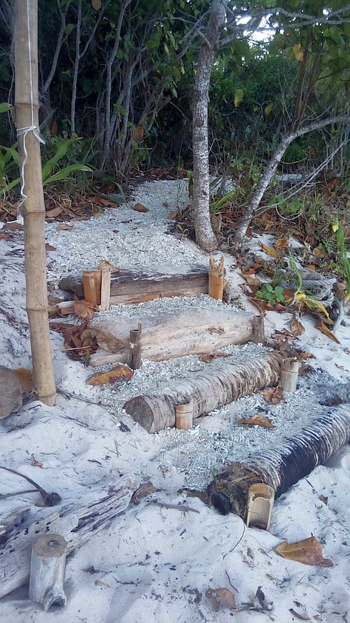 A rustic path made of wooden planks and gravel leads up a sandy slope, surrounded by trees and foliage. This inviting trail hints at hidden camping spots amidst the woods, offering a natural and serene beachside setting reminiscent of Palawan's tranquil landscapes.