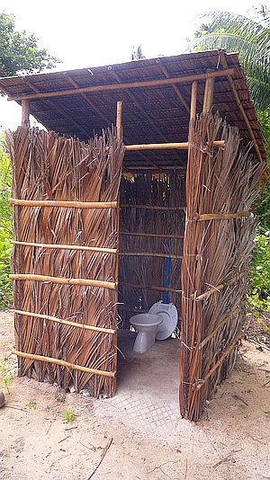 Rustic outdoor toilet with walls made of dried palm leaves and a simple roof, set on sandy ground—perfect for a quick stop during your boat tour.