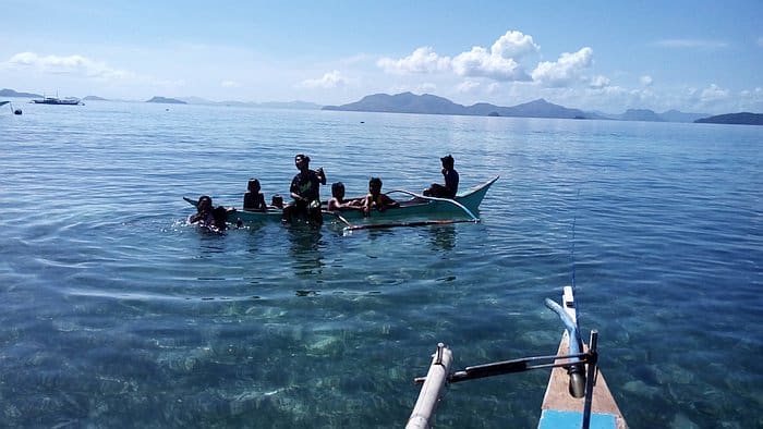 A group of people relishes the clear water during a delightful boat tour on a sunny day, with majestic mountains visible in the background.