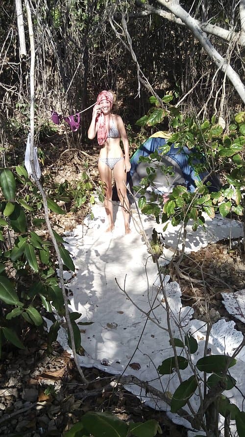 A person in swimwear stands on a towel in the forest, surrounded by greenery and sunlight, as if pausing between island hopping adventures.