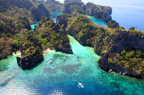 Aerial view of turquoise waters, rocky cliffs, and lush green islands in a tropical landscape, perfect for an El Nido boat tour adventure.