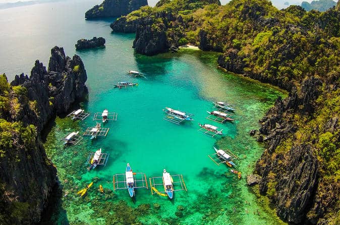 Aerial view of a turquoise lagoon in El Nido, surrounded by rocky cliffs with several boats from a boat tour gracefully floating on the water.