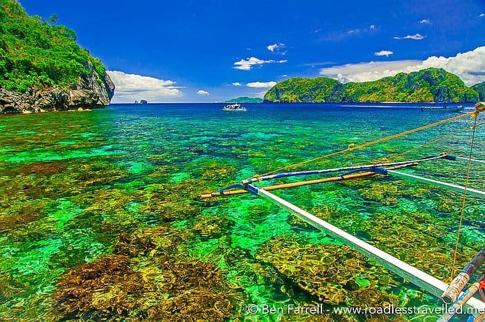 Experience the vibrant tropical seascape of El Nido with turquoise waters, lush green islands, and a boat's outrigger in the foreground—perfect for an unforgettable boat tour.